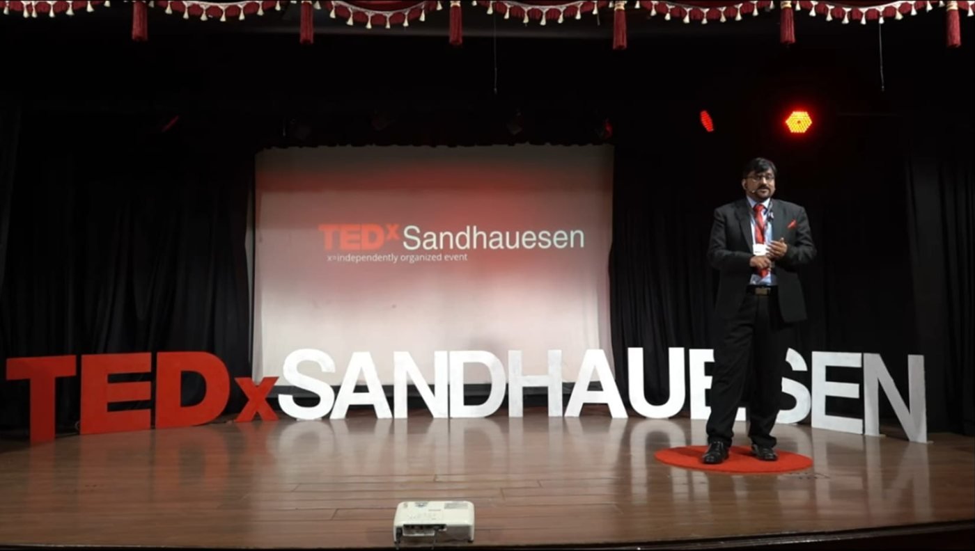 Dr. V J Nagesh speaking on the TEDxSandhauesen stage — watch the talk on YouTube
